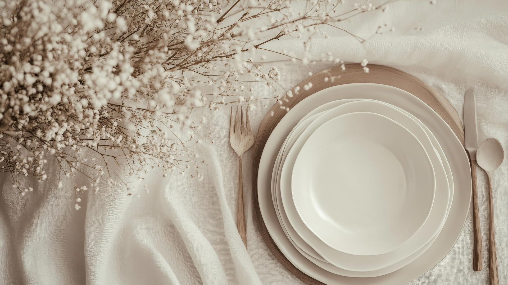 A minimalist Thanksgiving table setting with ceramic dishes, dried twigs, and beige textiles in a Scandinavian style.