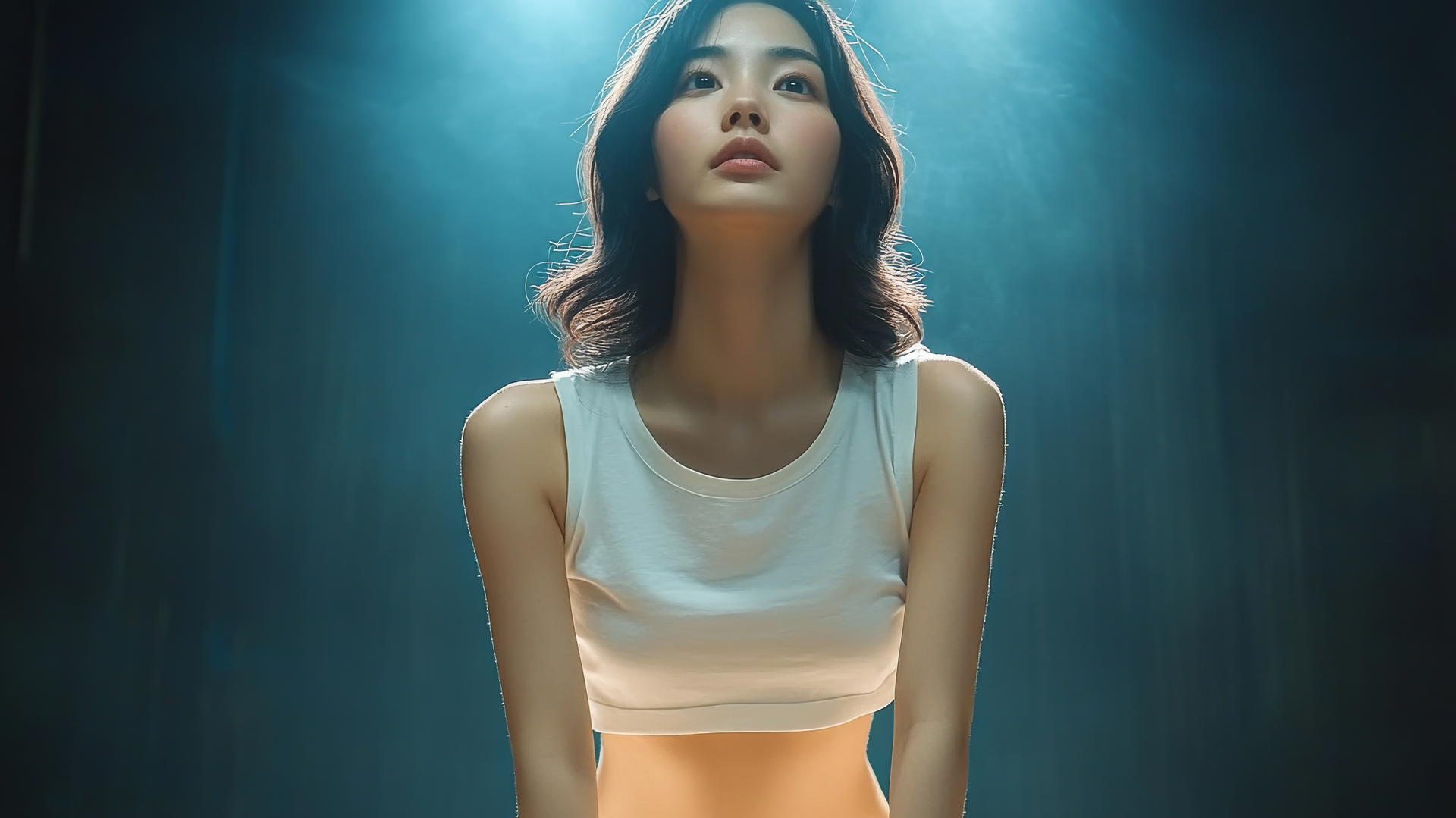 Low angle shot of an Asian girl kneeling, looking down, in a white t-shirt, waist focus.