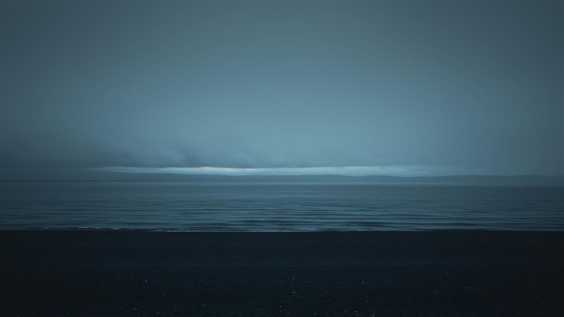 Dark overcast sky merging with sea at a black pebble beach