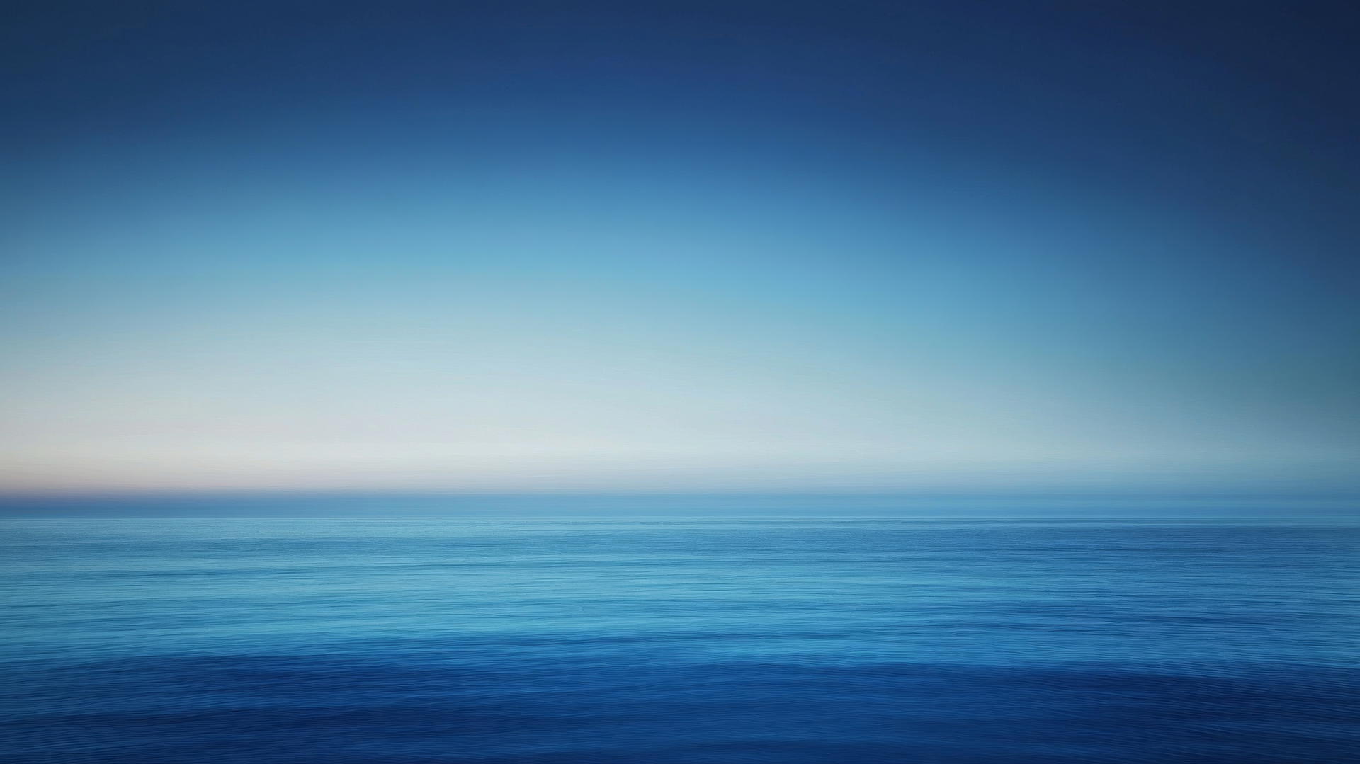 A gradient blue background wallpaper, from deep navy to light sky blue, ocean horizon at dusk.