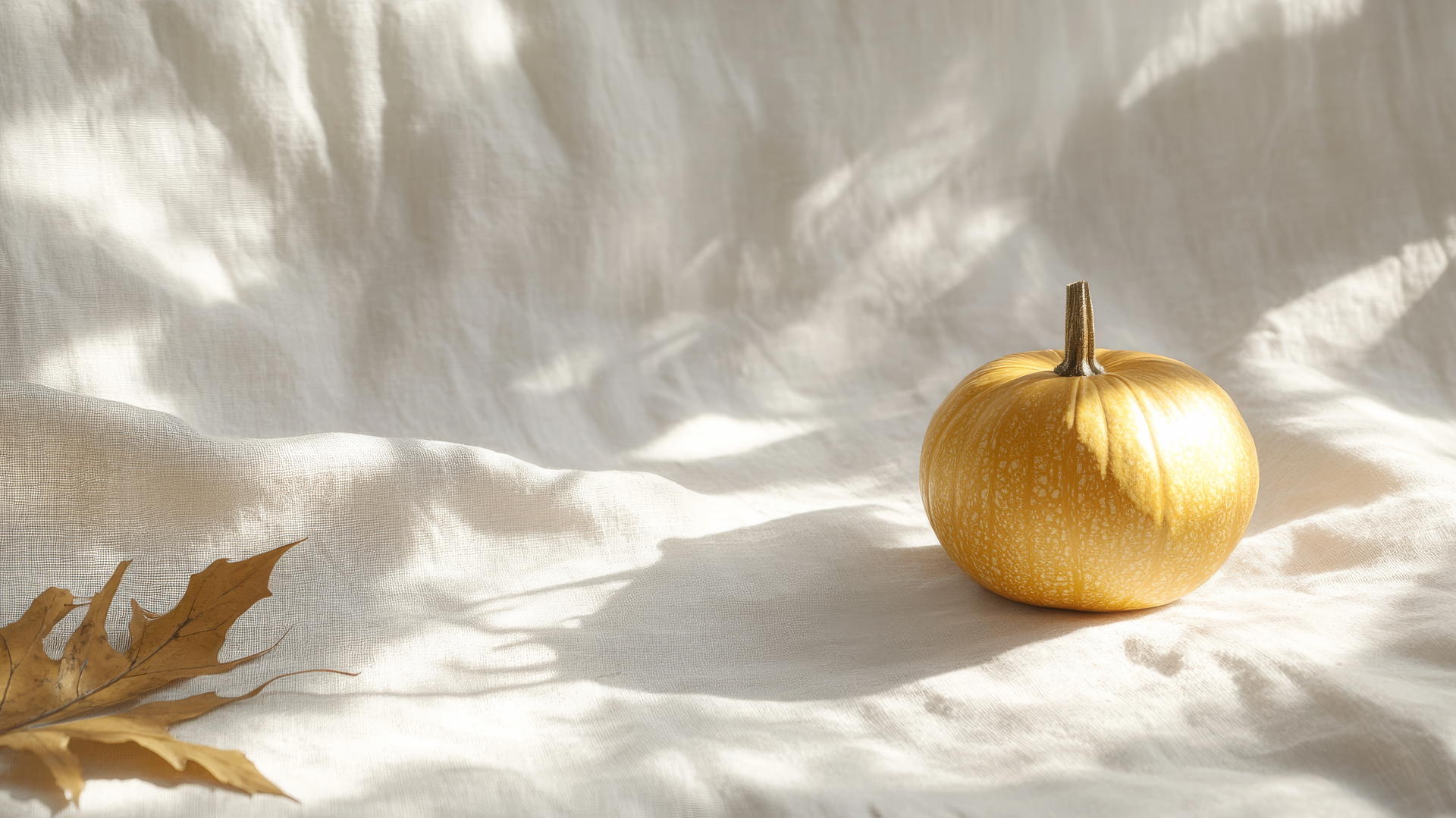 thanksgiving wallpaper aesthetic with a golden pumpkin on textured linen and dried leaves